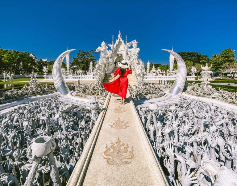 Tourist in red dress crossing bridge at Wat Rong Khun in Chiang Rai, Thailand